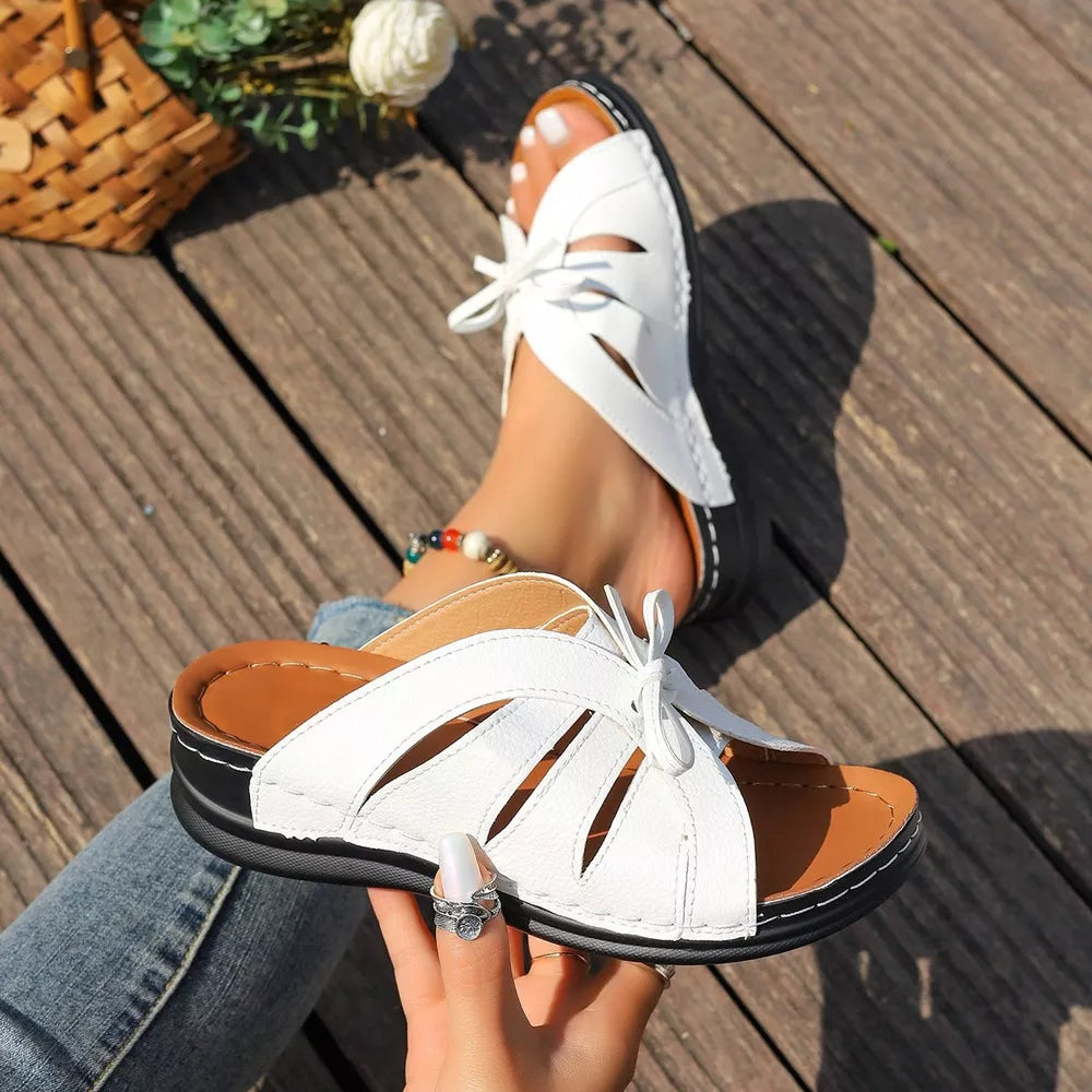 White criss-cross wedge sandals with cut-out details and a bow accent.