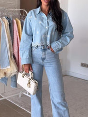 Light blue denim cropped shirt with floral embroidery and eyelet trim, worn by a woman.