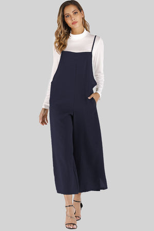 Dark navy culotte overalls with slender straps and wide legs, worn over a white turtleneck.