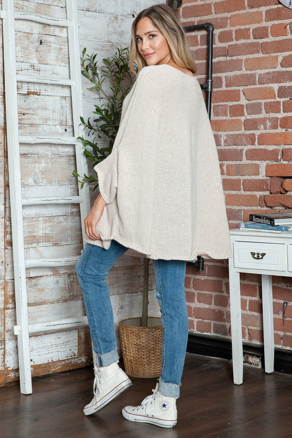Cream knit sweater with relaxed fit and cape sleeves, styled with jeans.