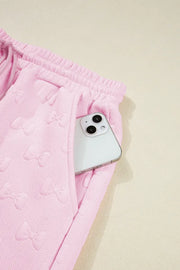 Blush pink loungewear set with embossed bow pattern and side pocket holding a phone.