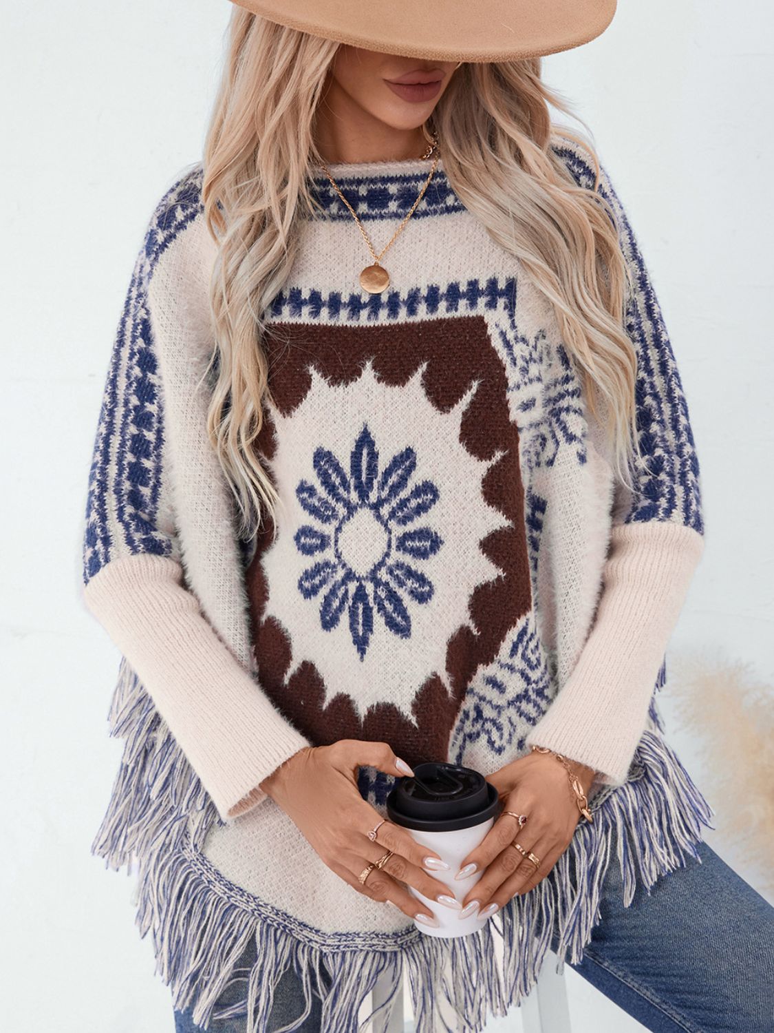 Cream acrylic poncho with Aztec motif, fringe detail, and long sleeves.
