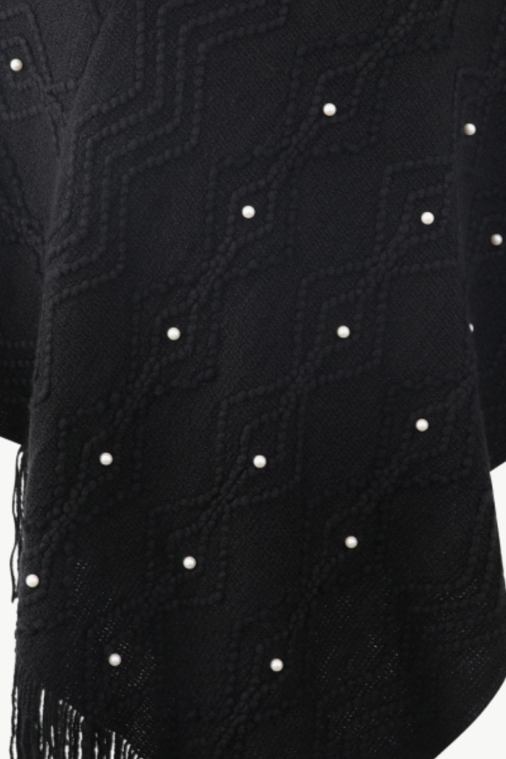Black knit poncho with geometric pattern and pearl embellishments, featuring fringe detail.