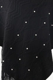 Black knit poncho with geometric pattern and pearl embellishments, featuring fringe detail.