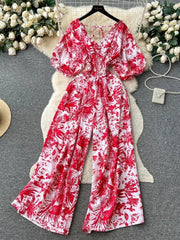 Scarlet tropical print smocked wide-leg maternity romper with puff sleeves and tie neck.