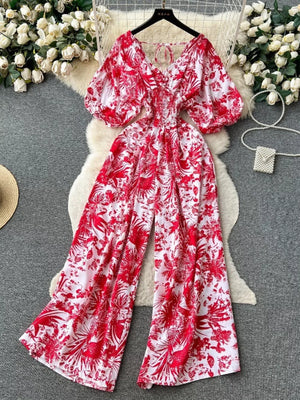 Scarlet tropical print smocked wide-leg maternity romper with puff sleeves and tie neck.