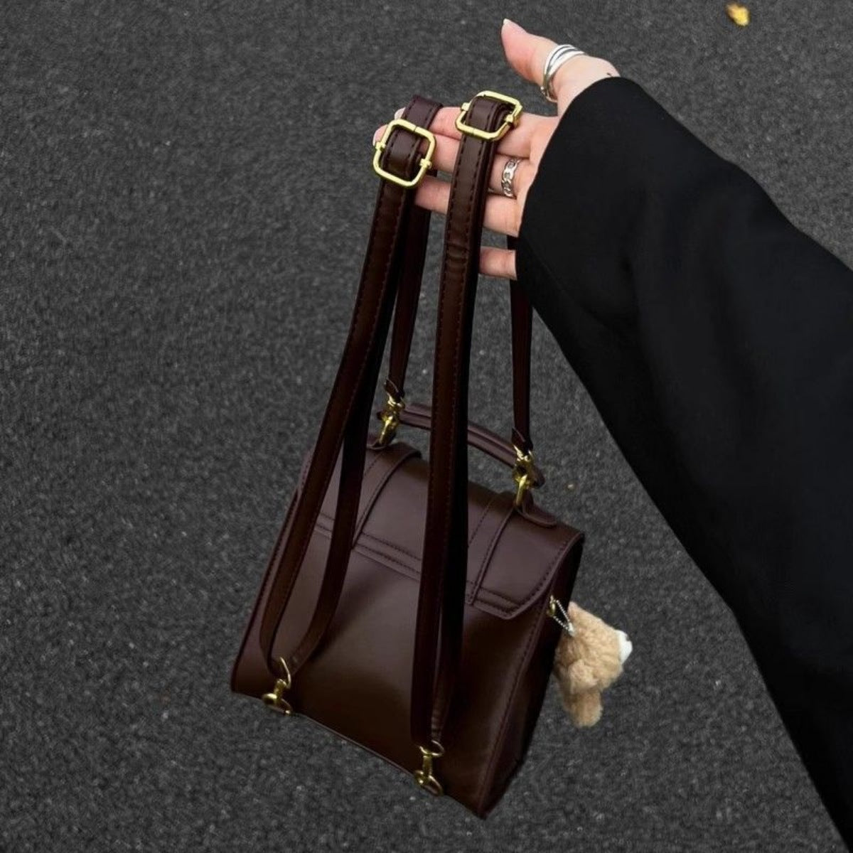 Mini brown pu leather backpack with decorative straps and gold hardware, a small teddy bear charm hangs from the side.