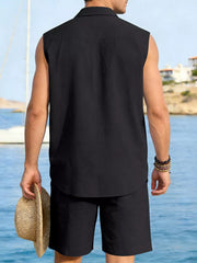Men's black sleeveless linen shirt and shorts set, holding straw hat.