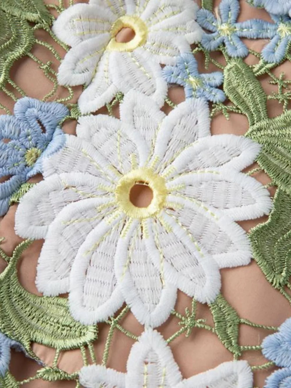 Embroidered floral maxi dress detail with white, blue, and green appliqué flowers and leaves on a peach background.