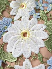 Embroidered floral maxi dress detail with white, blue, and green appliqué flowers and leaves on a peach background.