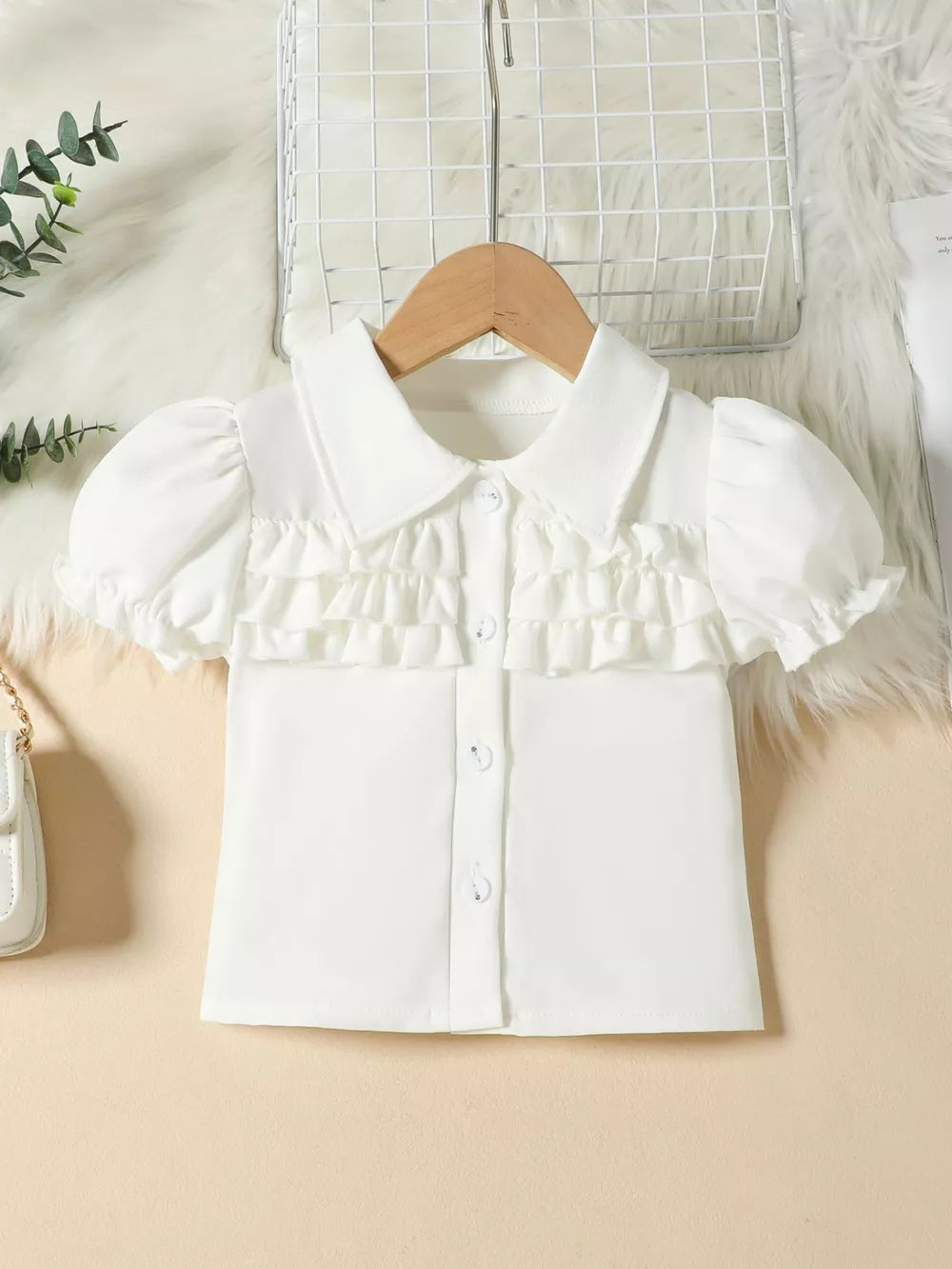 White baby top with puff sleeves, ruffled front, and button closure.