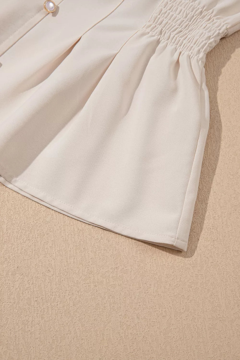 Elegant V-neck polyester blouse with smocked waist detail and pearl button.