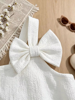 White baby dress with textured fabric and large bow detail on strap.