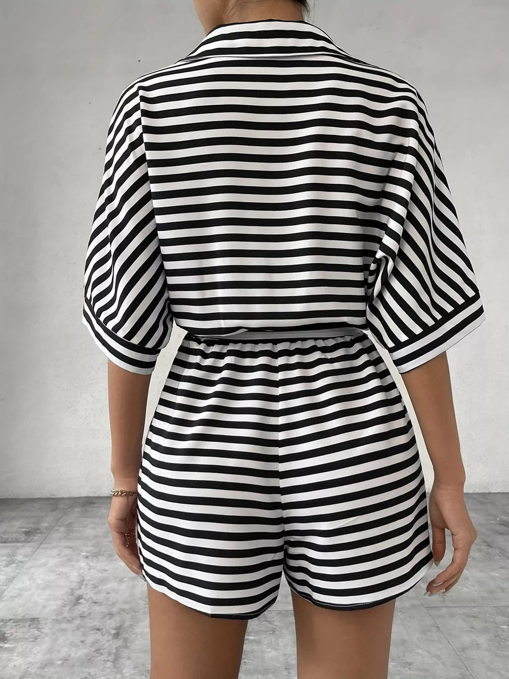 Black and white striped belted romper with collared button-front top and elastic waist shorts.