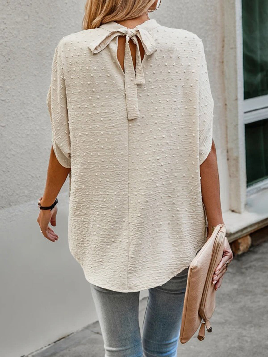 Cream textured dot back-tie blouse with short sleeves and a bow detail.