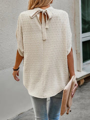 Cream textured dot back-tie blouse with short sleeves and a bow detail.