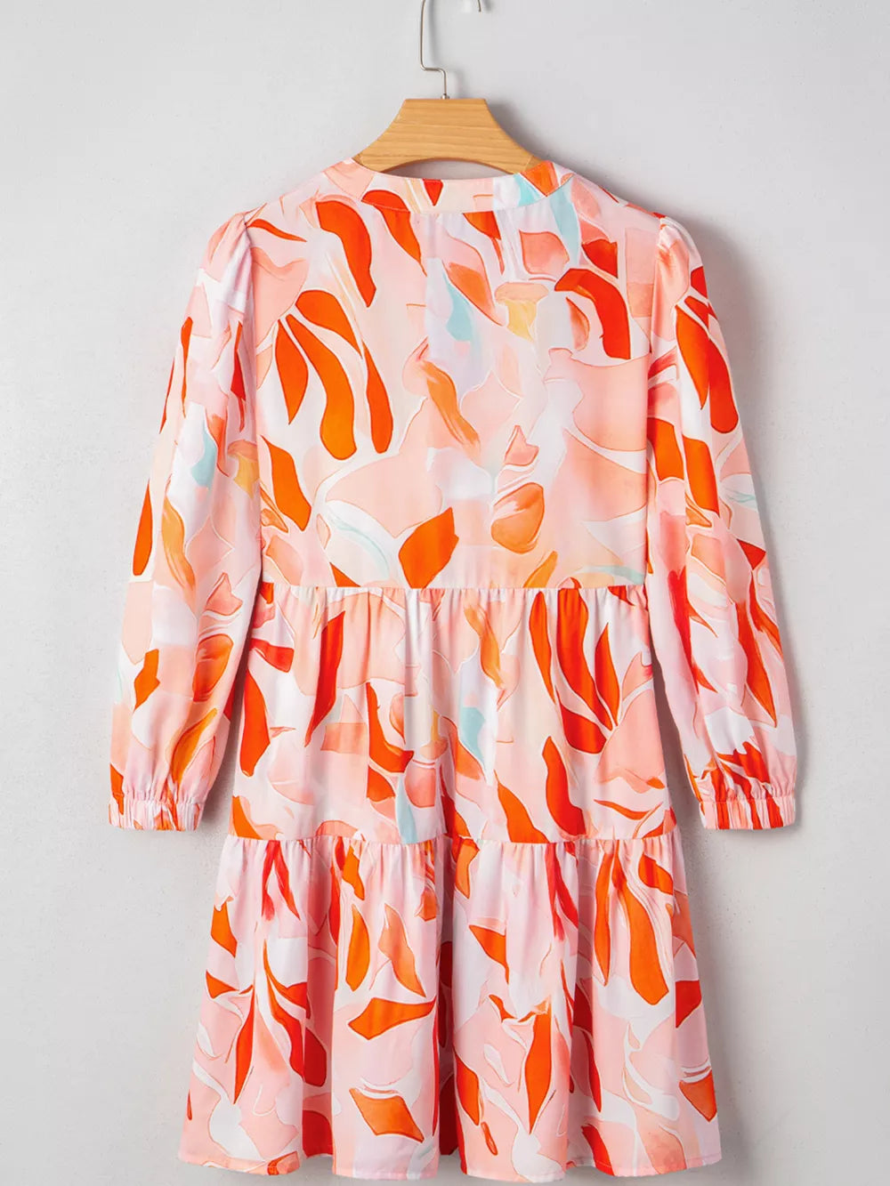 Tiered mini dress with abstract print, long sleeves, and a ruffled hem in pink and orange.