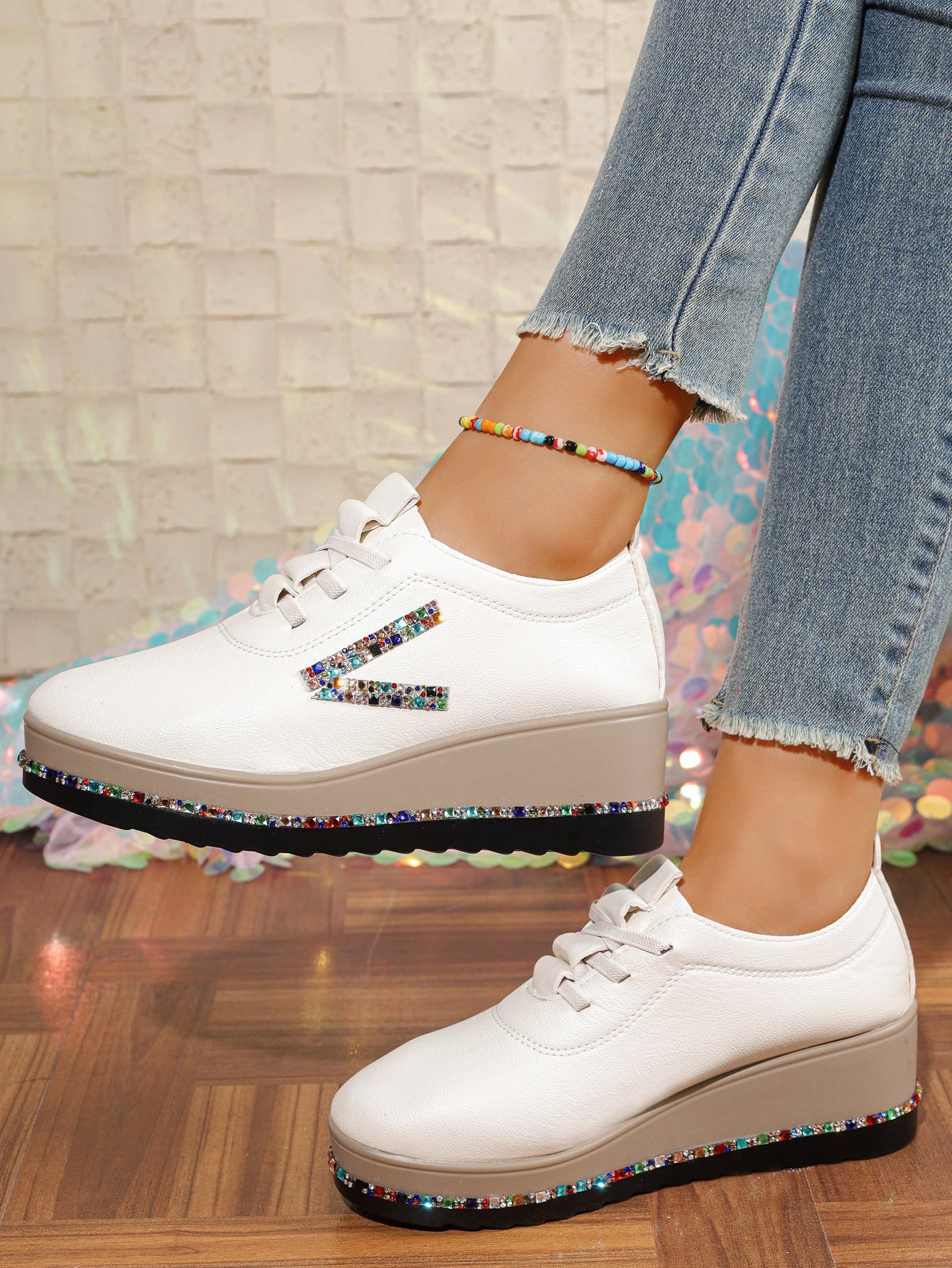 White wedge sneakers with rhinestone embellishments on the side and sole.