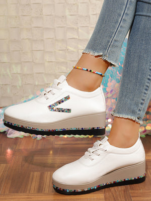 White wedge sneakers with rhinestone embellishments on the side and sole.
