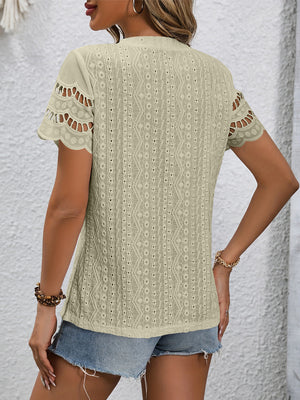 Beige eyelet blouse with scalloped short sleeves and intricate patterned fabric.