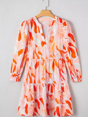 Vibrant abstract print tiered mini dress with V-neck and long sleeves.