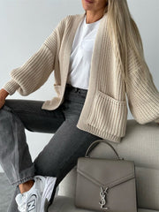 Beige textured knit cardigan with puff sleeves and pockets, styled with a white tee and jeans.