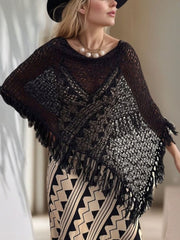 Black open-knit poncho with boat neck and fringe trim, styled over a patterned dress.