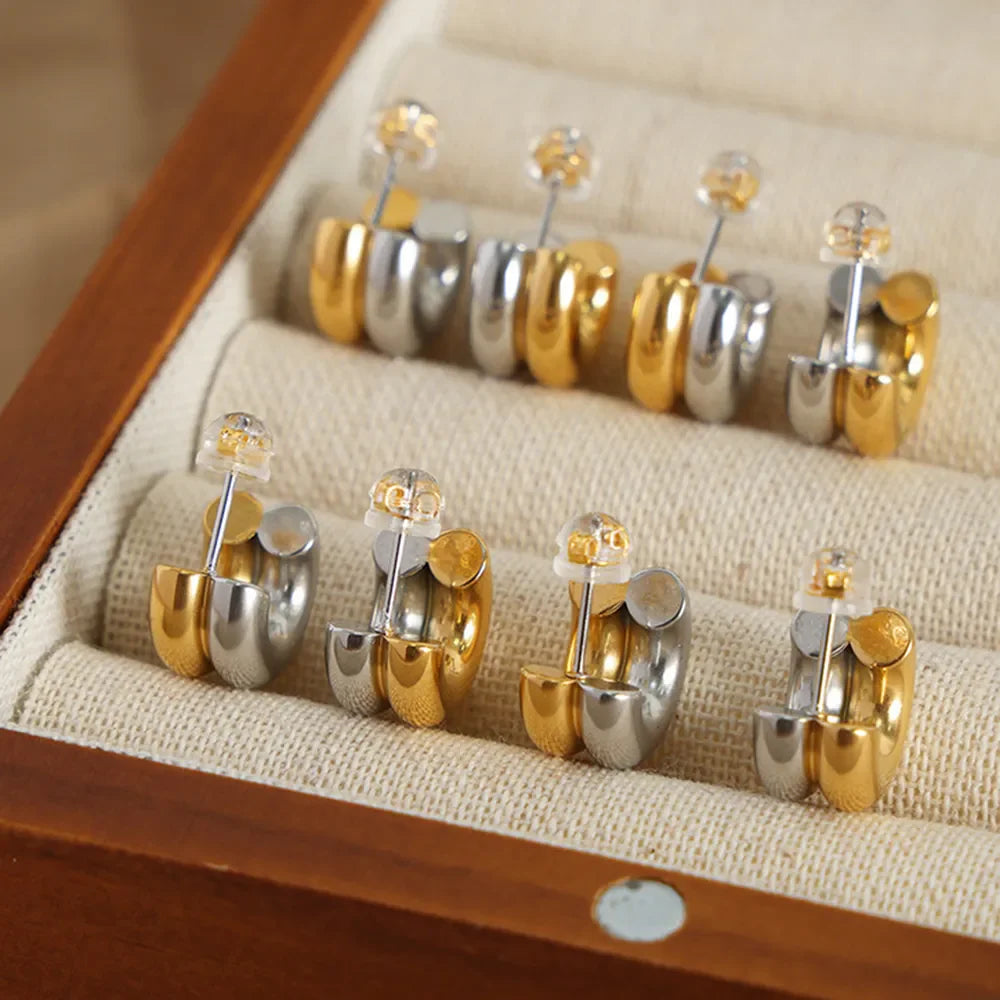Dual-tone sculptural C-hoop earrings in gold and silver, shown in a jewelry box.