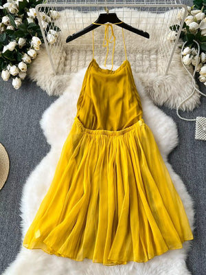 Yellow halter neck backless dress with a flowy pleated skirt.