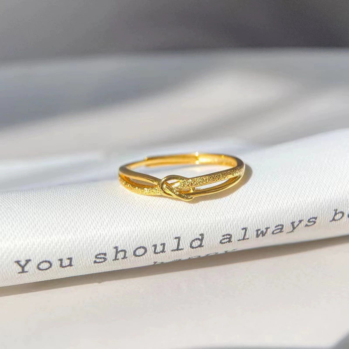 Gold knot ring with textured detail on a white surface with text.