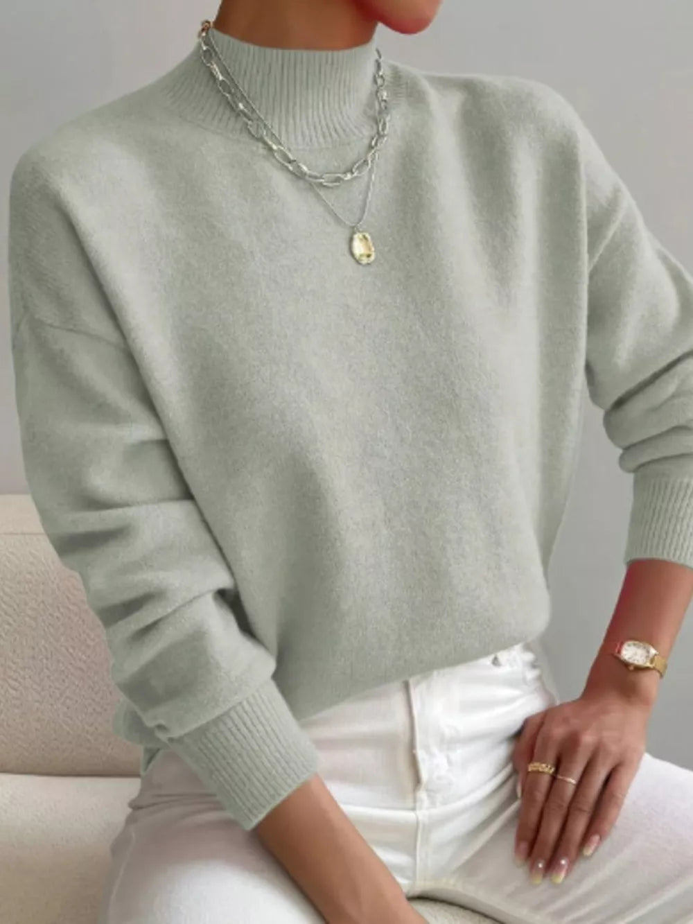 Light gray mock neck knit sweater with dropped shoulders, styled with layered necklaces.