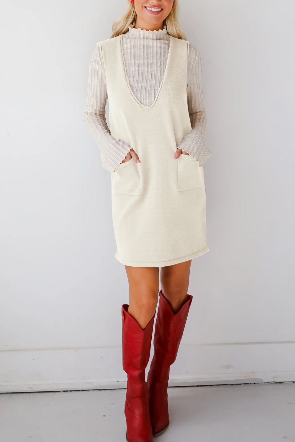 Cream sleeveless knit dress with V-neck and patch pockets, styled with a long sleeve top.