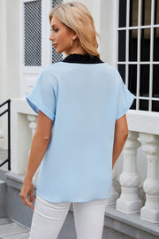 Light blue blouson top with black contrast V-neck and cuffed short sleeves.