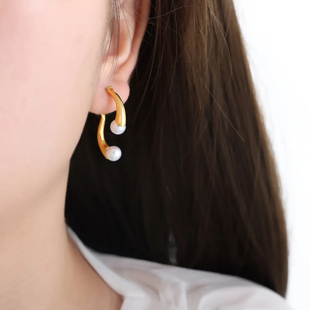 Gold sculptural pearl drop hoop earrings with a modern curved design.