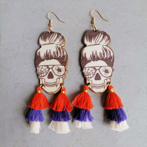 Skull bun drop earrings with orange, purple, and white tassels and spiderweb glasses.