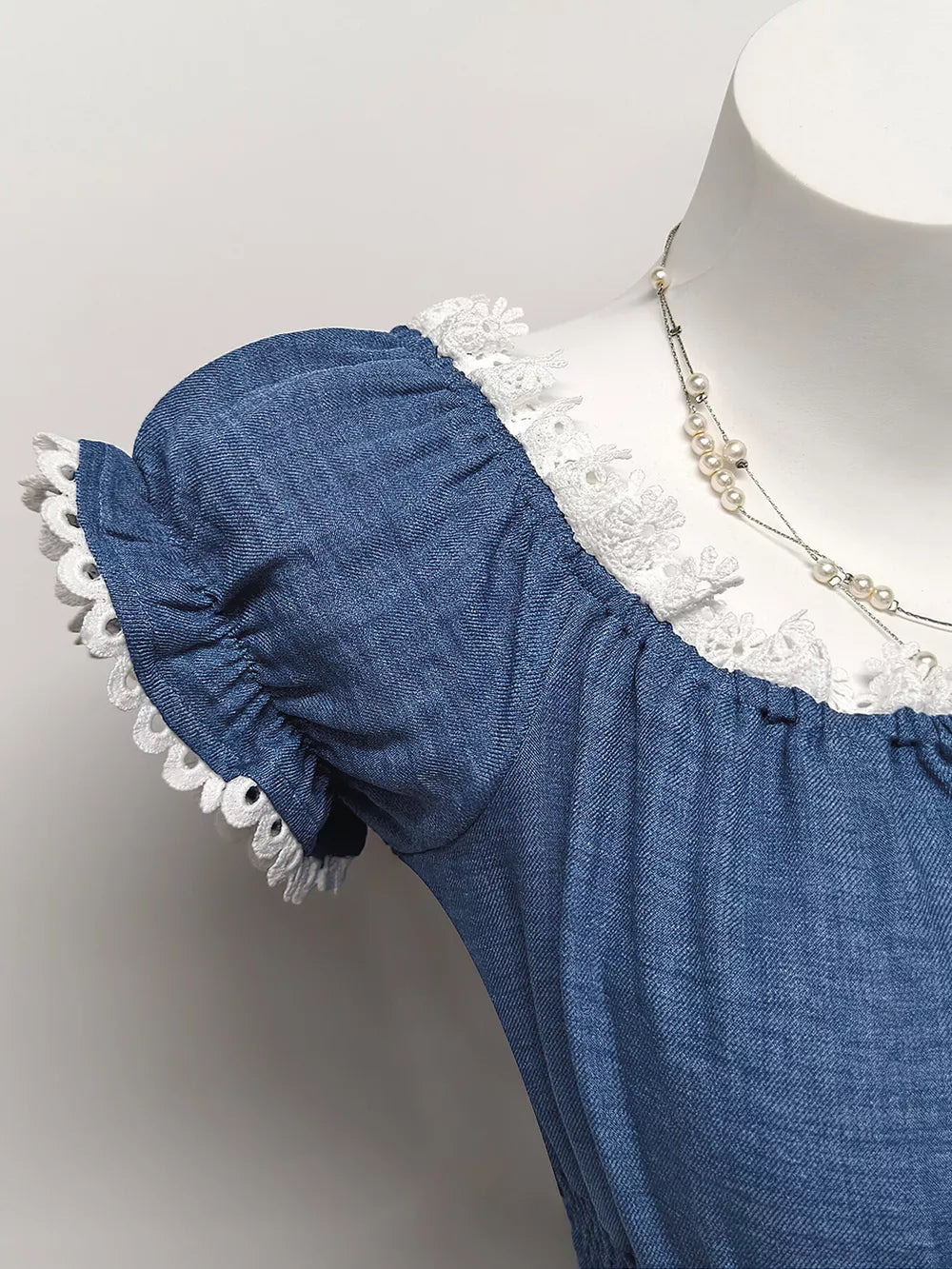 Blue denim maternity blouse with smocked neckline, puff sleeves, and eyelet trim.