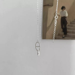 Silver necklace with oval geometric pendant adorned with cubic zirconia and a small leaf charm.