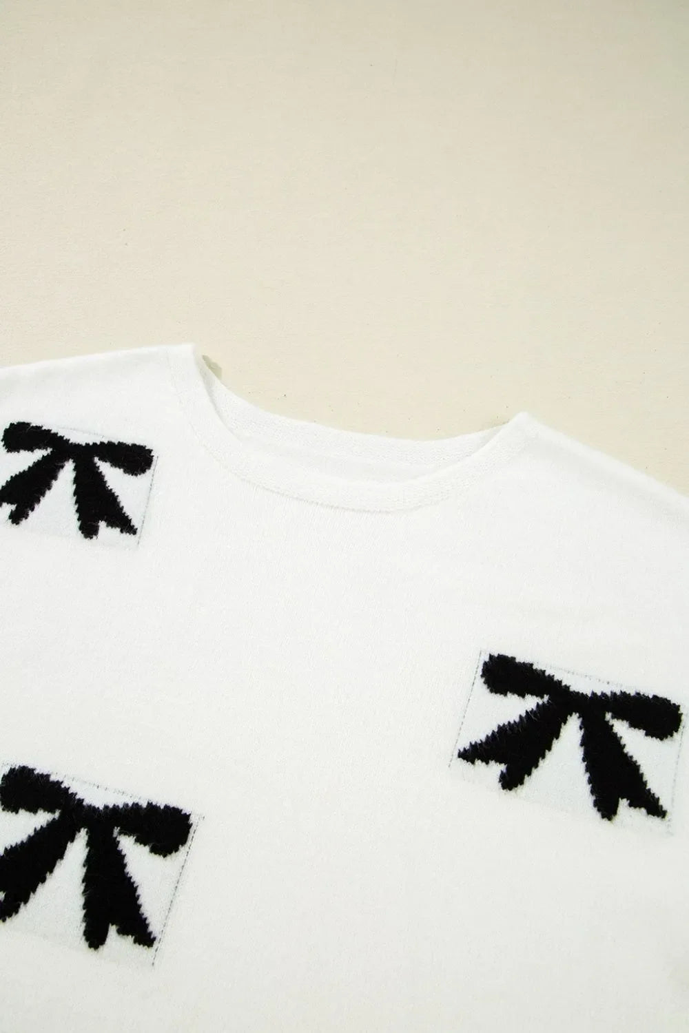 White knit tunic with black bow motif pattern and crew neck.