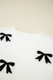 White knit tunic with black bow motif pattern and crew neck.
