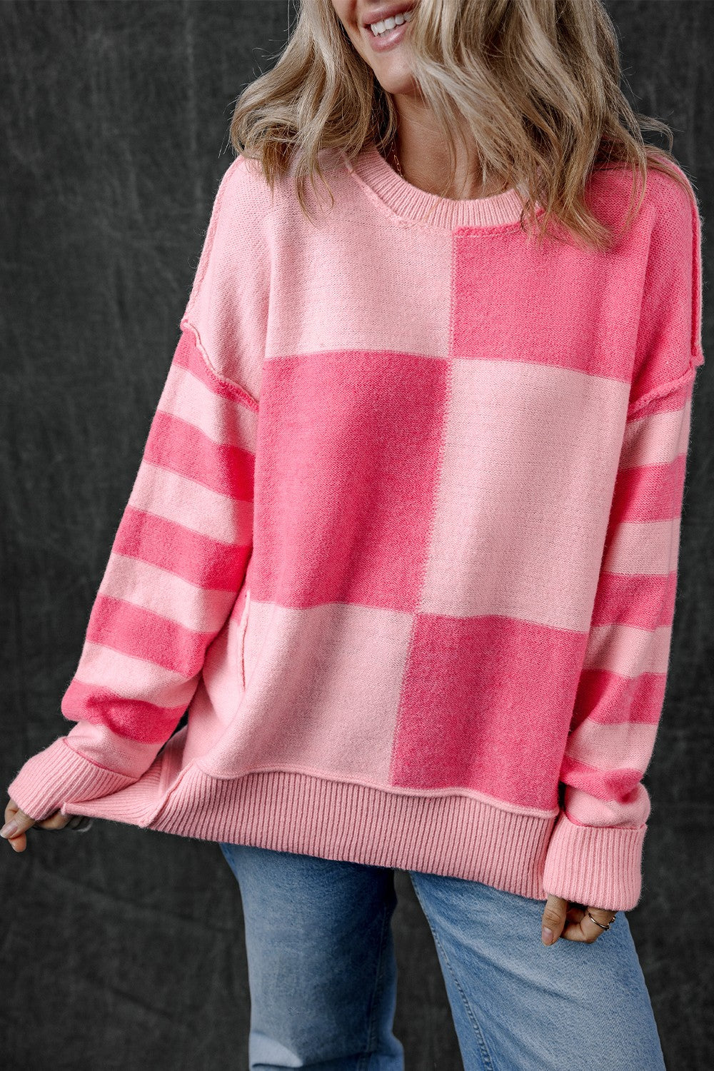 Checkerboard knit crewneck sweater in blush pink with striped sleeves and ribbed trim.