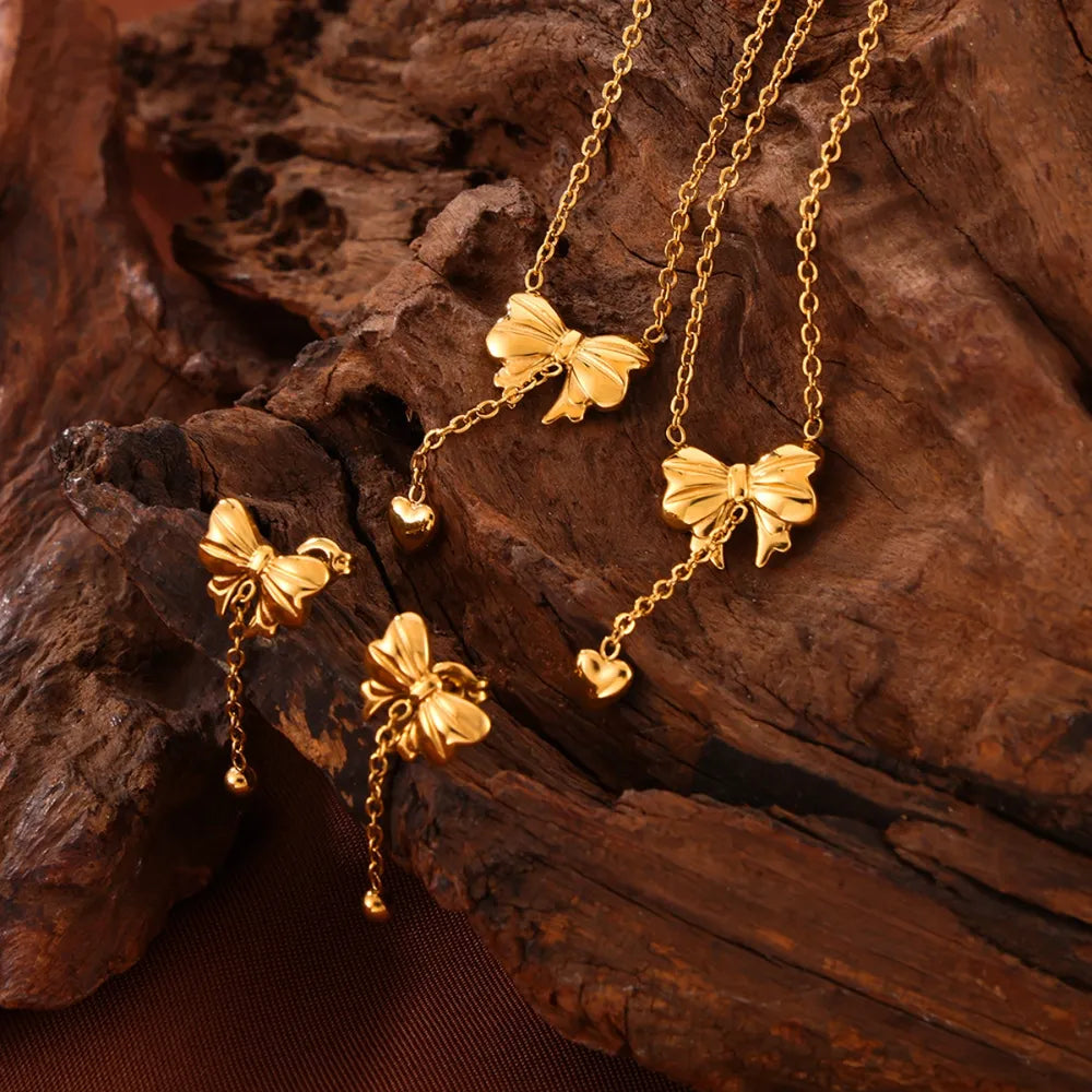 Gold bow drop chain earrings with heart charms and bead details.