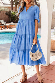 Blue tiered midi dress with notched neckline and tie-sleeve detail.