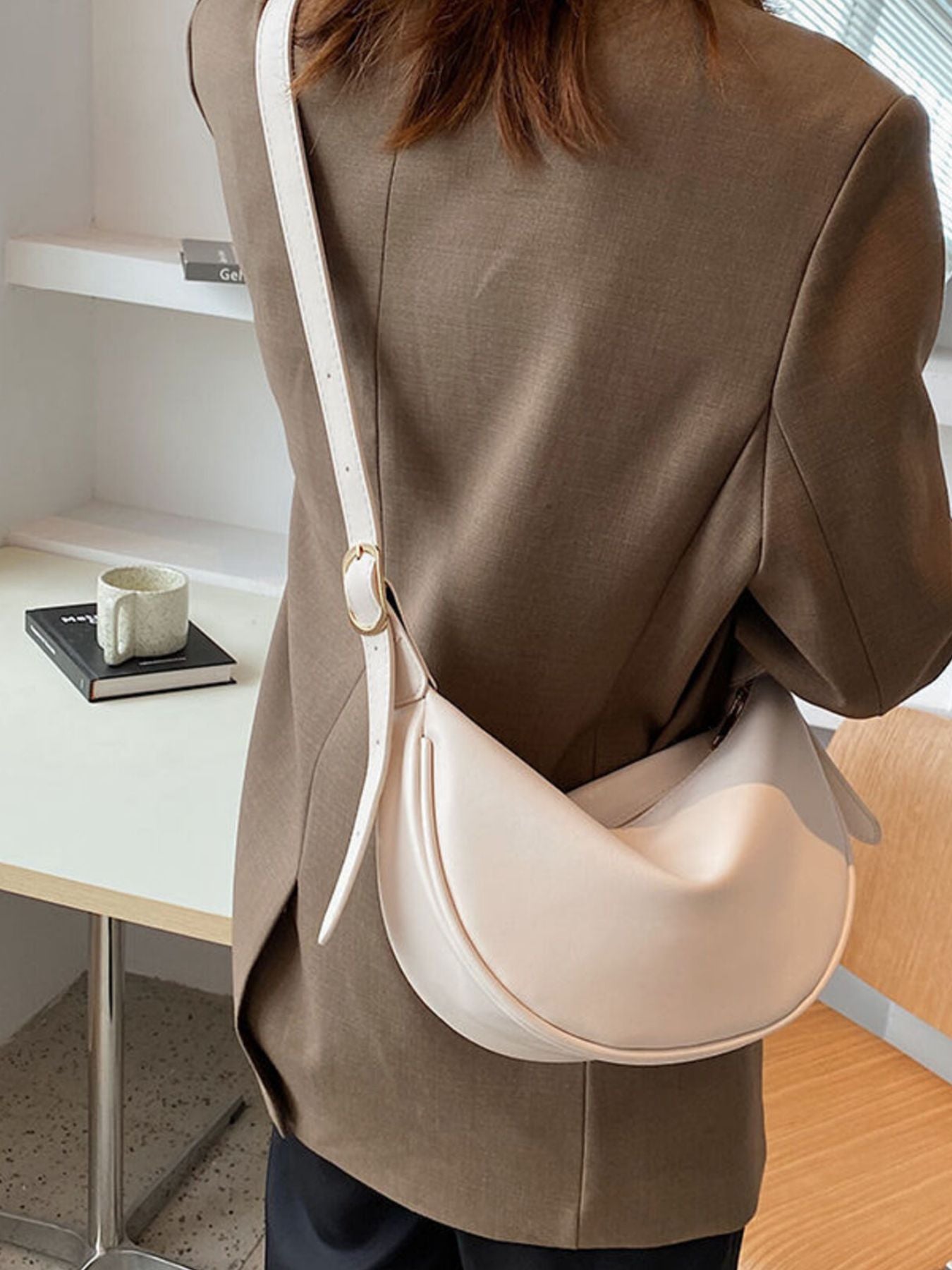 Crescent crossbody bag in beige white faux leather with adjustable strap.