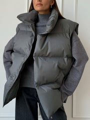 Padded puffer vest in dark gray with a high collar and zip front, worn over a gray turtleneck.