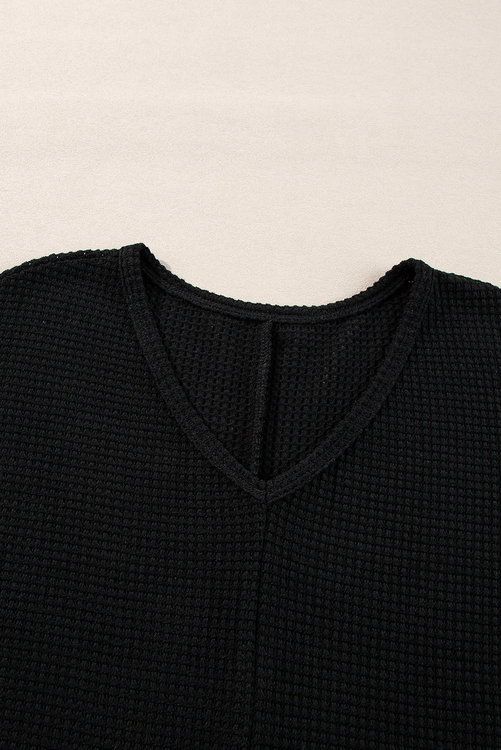 Black waffle knit V-neck top with a subtle slit detail at the neckline.