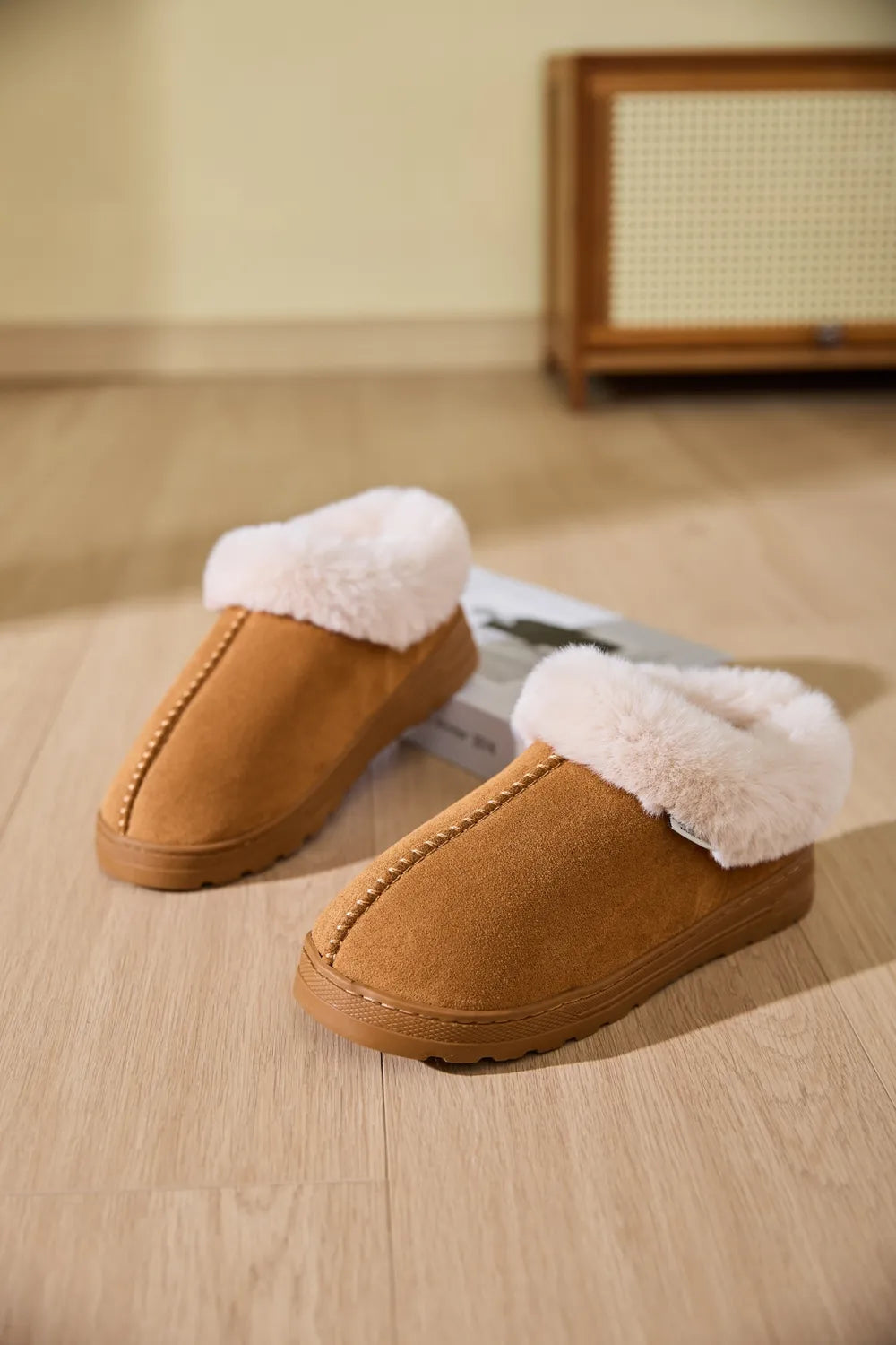 Caramel suede house slippers with plush shearling trim and decorative stitching.