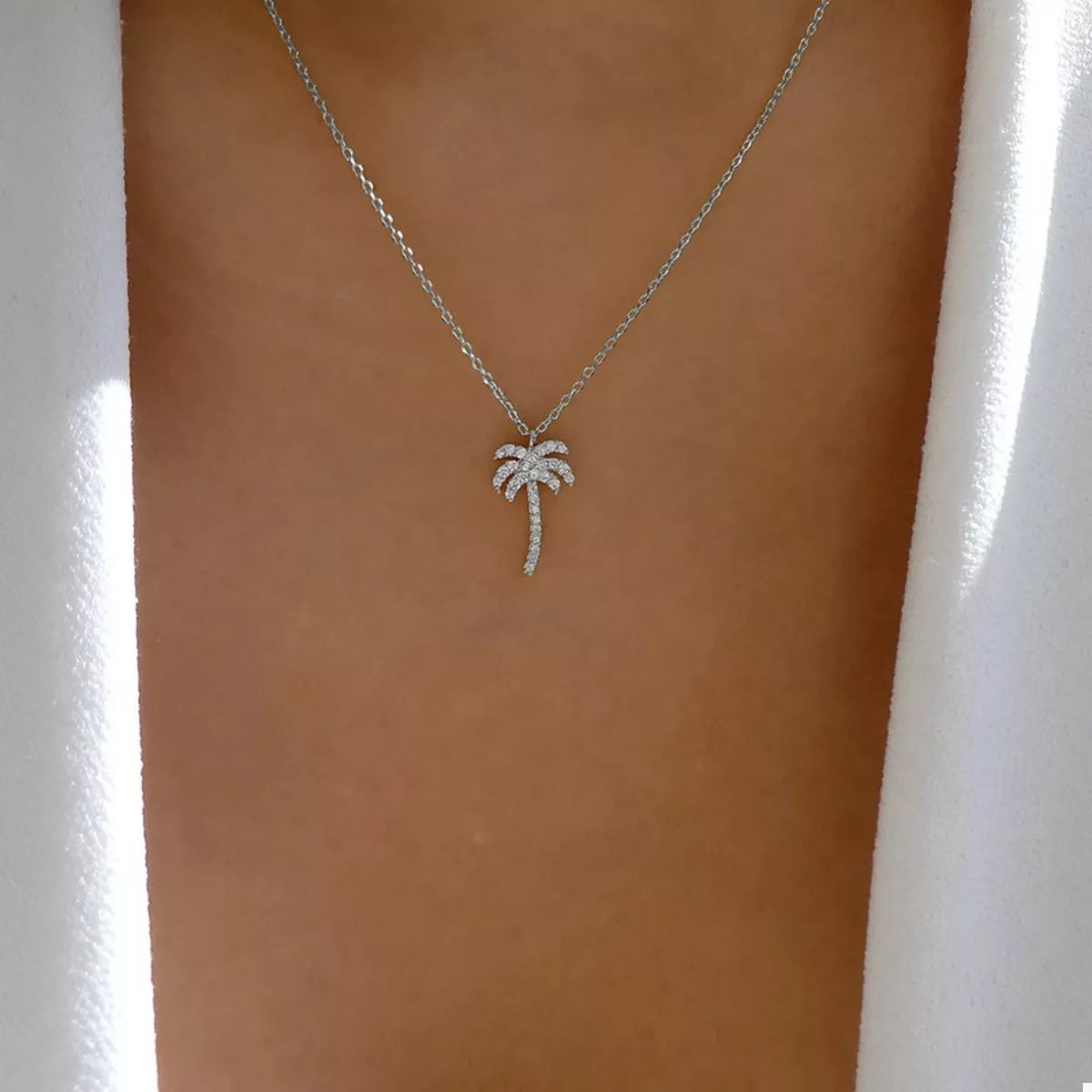 Silver palm tree pendant necklace with crystal accents on a delicate chain.