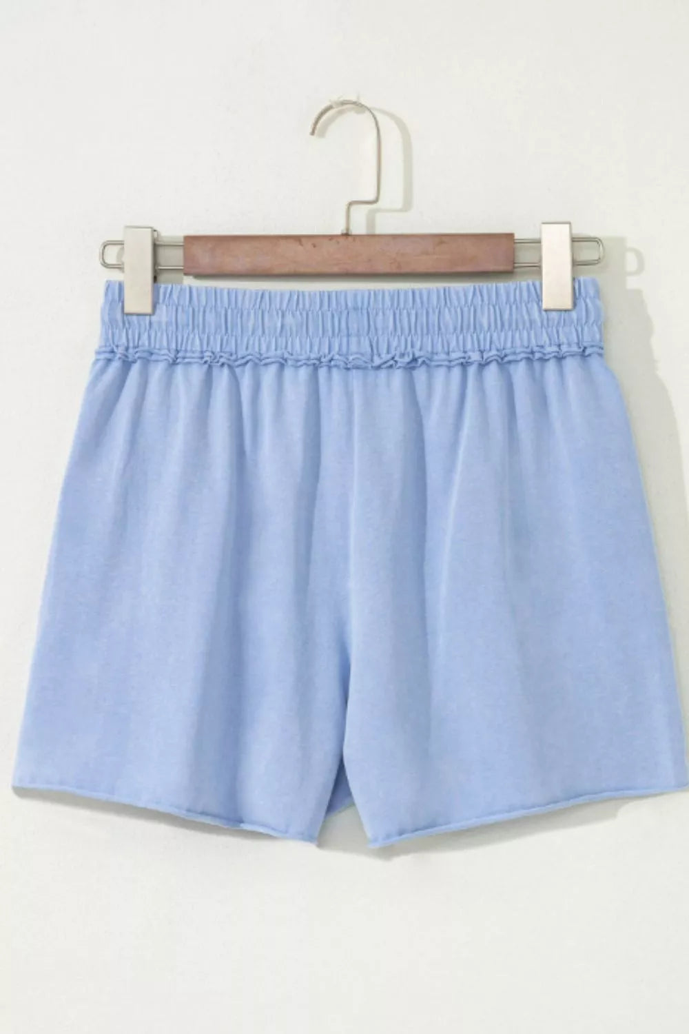 Light blue cotton drawstring shorts with elastic ruffled waist and raw hem.