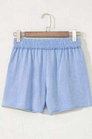 Light blue cotton drawstring shorts with elastic ruffled waist and raw hem.