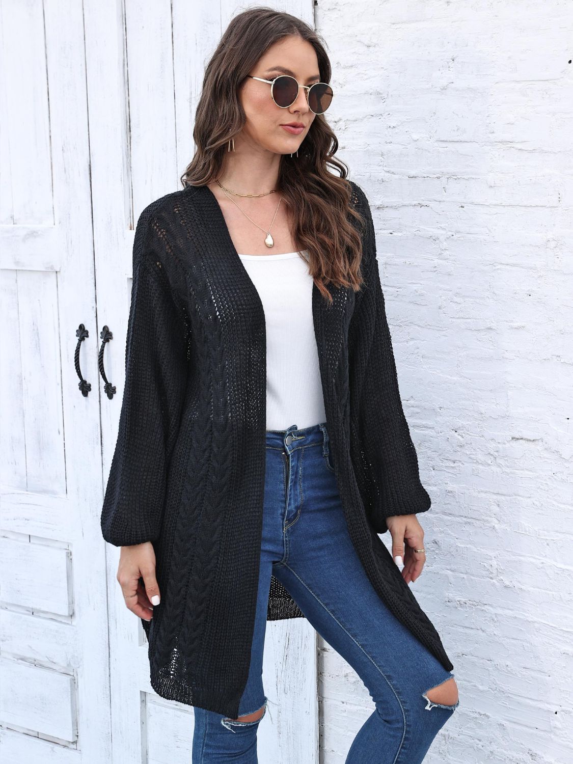 Black cable knit cocoon cardigan with V-neck and long sleeves.